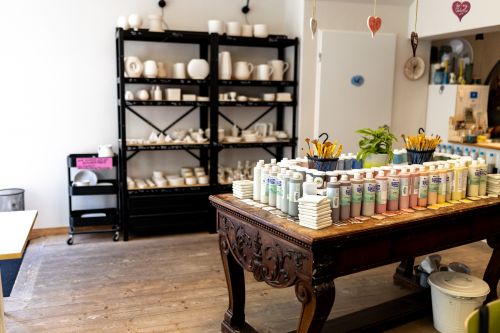 Bild eines Raumes in der Keramik-Werkstatt Keramiktraum mit einem Tisch mit vielen Farben und einem Regal mit Rohlingen, einer Kooperationslocation vom Schärferaum, einer Mietlocation in Bad Homburg bei Frankfurt am Main für Team-Events, Veranstaltungen, Workshops, Tagungen und Firmen.